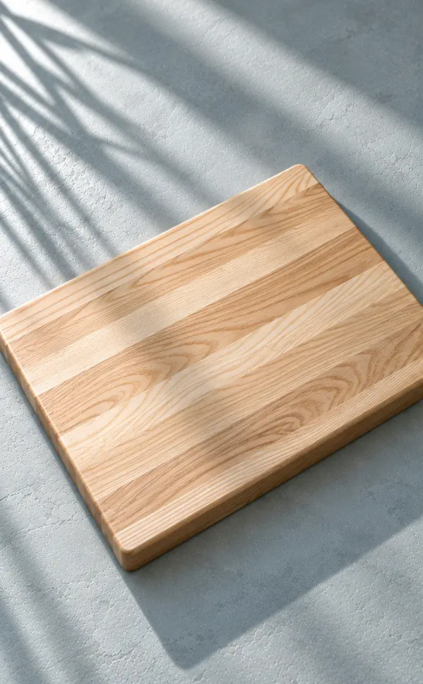 Pale edge-grain ash chopping board on a muted blue-grey surface