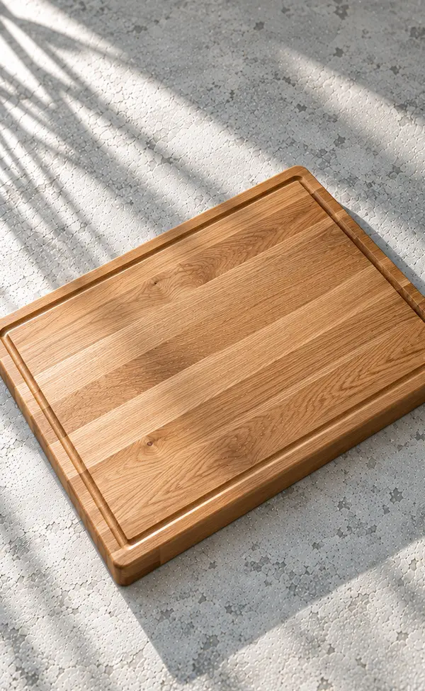 Large edge-grain oak chopping board with a shallow juice groove on a pale stone surface