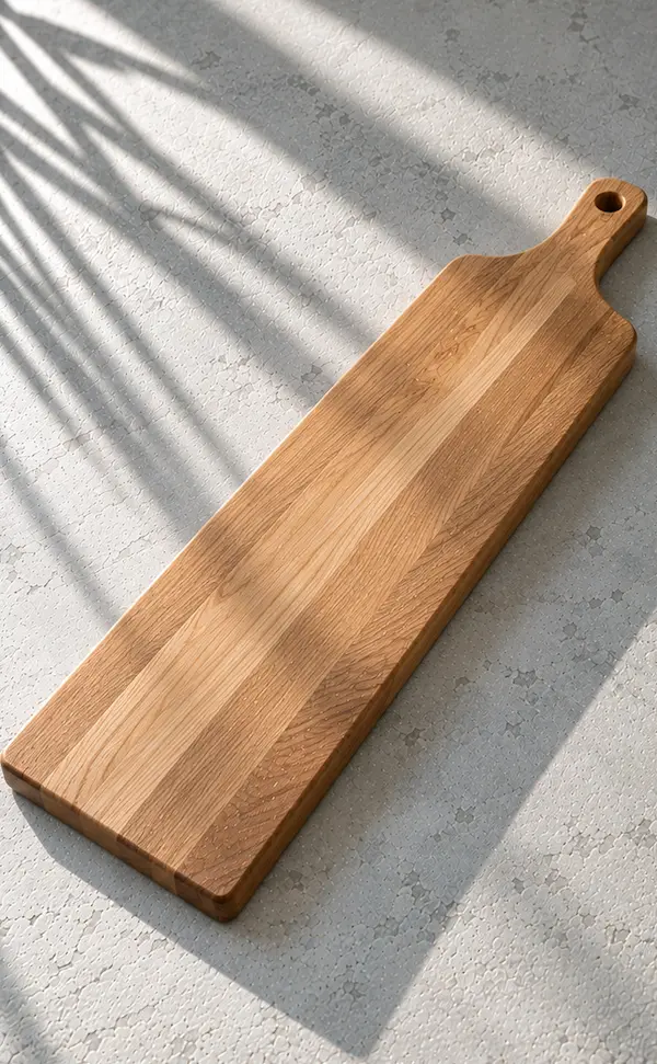 Long narrow oak serving board with a shaped grip on a pale stone surface