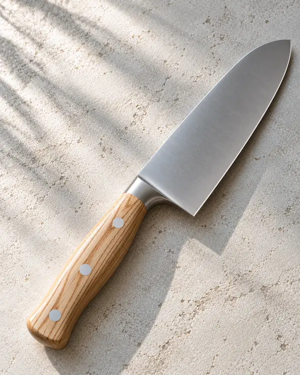 Santoku knife with a pale ash handle resting on chalk-coloured plaster